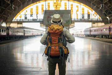 Mann mit Hut und Rucksack von hinten in einem Bahnhof