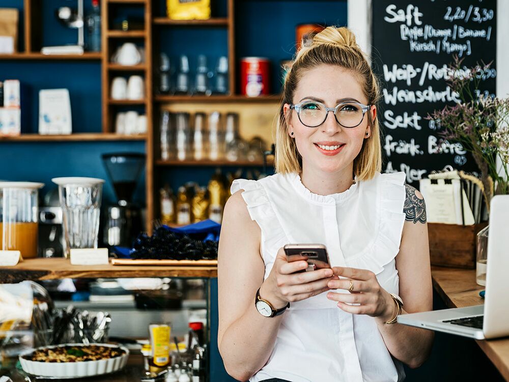 Frau steht in ihrem Geschäft und hält Smartphone in der Hand 