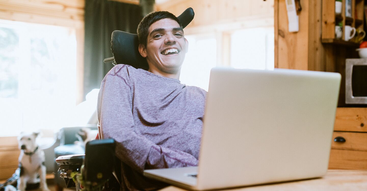 Mann in Rollstuhl am Laptop lächelnd