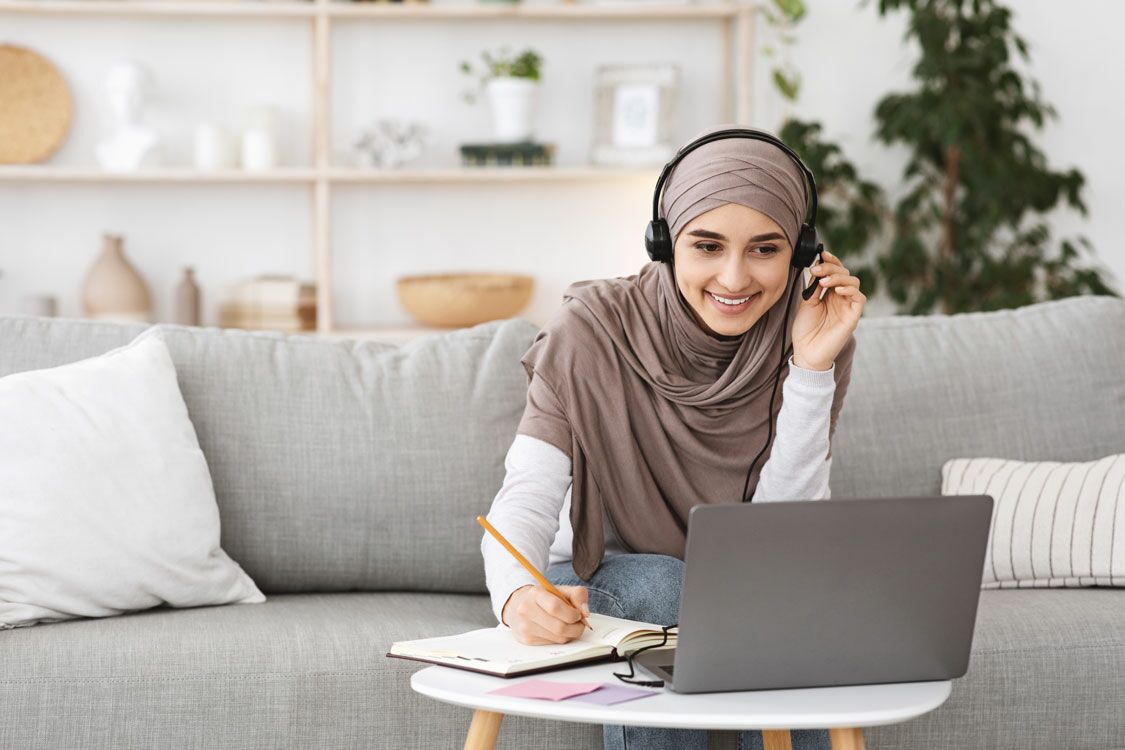 Frau mit Headset im Wohnzimmer am Laptop und Notizblock