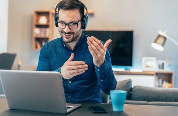 Gestikulierender Mann mit Kopfhörern vor Notebook