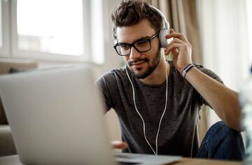 Junger Mann mit Kopfhörern sitzt an Tisch vor Notebook