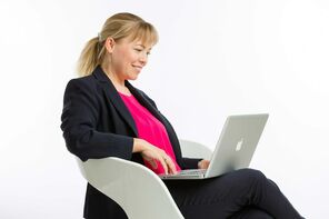 Frau in Businessoutfit sitzt auf Stuhl und hat Notebook auf dem Schoß.