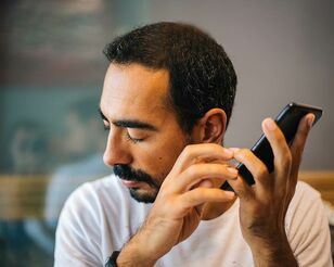Mann mit geschlossenen Augen hört Tonaufnahmen am Smartphone