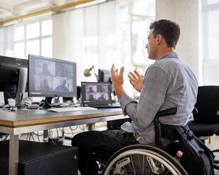 Mann im Rollstuhl vor Bildschirmen nimmt an Webinar teil und diskutiert