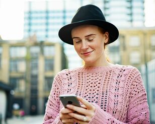 Junge Frau mit Hut blickt auf Smartphone und lächelt