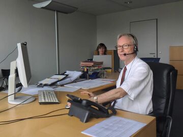 Mann an PC mit Headset im Vordergrund, Frau an Notebook im Hintergrund in Büro