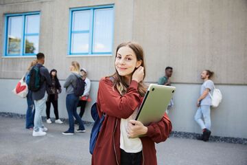 Frau steht vor einem Gebäude mit einem Laptop in der Hand und lächelt in die Kamera