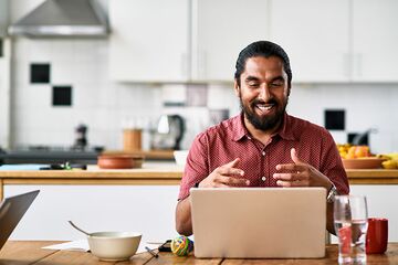 Ein dunkelhäutiger Mann sitzt gestikulierend vor seinem Laptop in der Küche