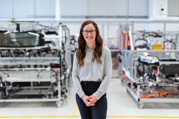 Eine Frau steht in einer Produktionshalle und lächelt in die Kamera
