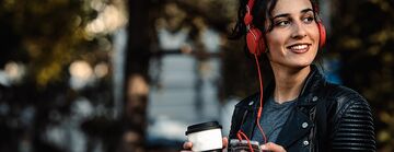 Dunkelhaarige Frau mit roten Kopfhörern hört über ihr Smartphone