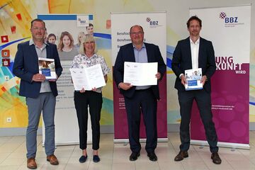 Gruppenbild mit vier Personen vor Roll-Ups, die Dokumente in den Händen halten