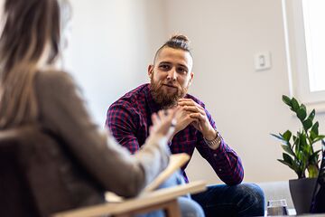 Mann sitzt auf einer Couch und wird von einer Studienzentrums-Mitarbeiterin beraten.