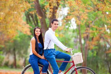 Junge Frau und junger Mann sitzen auf Tandem im herbstlichen Wald und schauen in Kamera