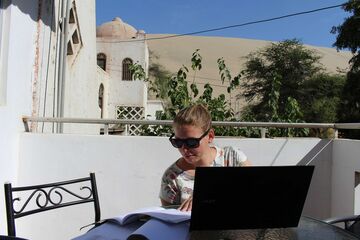 Bettina Mandel auf einem Balkon vor einem Laptop sitzend 