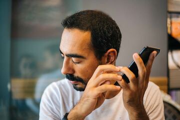 Mann mit geschlossenen Augen hört Tonaufnahmen am Smartphone