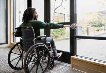 Mann in Rollstuhl betätigt automatischen Türöffner