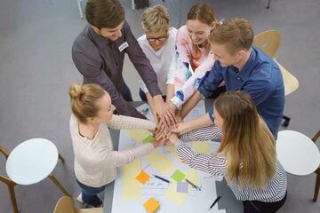 Eine Gruppe Studierender die sich während einer Präsenzveranstaltung die Hände geben