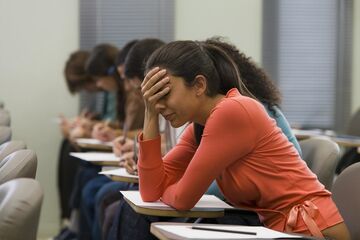 Studentin sitzend beugt sich am Tisch nach vorne und hält die Hand vor ihr Gesicht