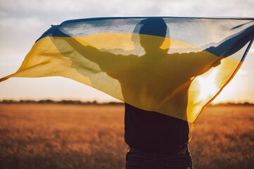 Mensch mit ukrainischer Fahne über Schultern steht auf Feld